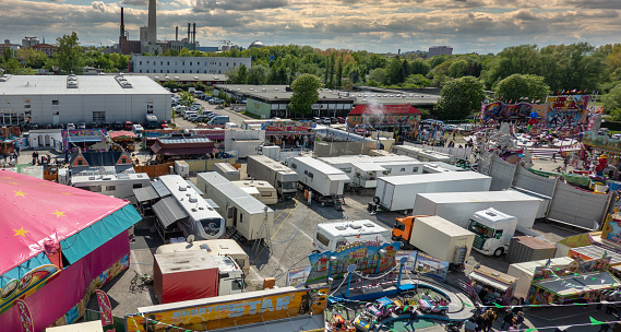 Braunschweig, Germany, May 5., 2019: Aerial view of the caravans of the carnies standing behind the rides of a fairground. A combined heat and power plant with a long chimney in the back