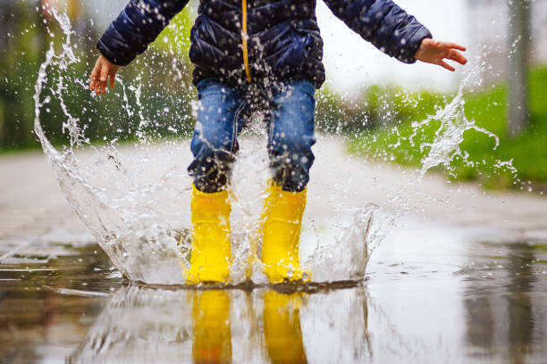 le gambe ravvicinate del bambino con stivali di gomma gialla saltano nella pozzanghera durante una passeggiata autunnale - pioggia foto e immagini stock