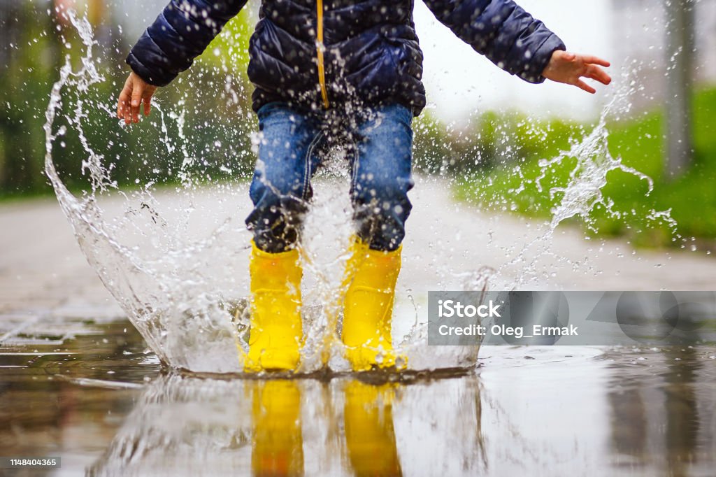 Close up legs of child with yellow rubber boots jump in puddle on an autumn walk Rain Stock Photo