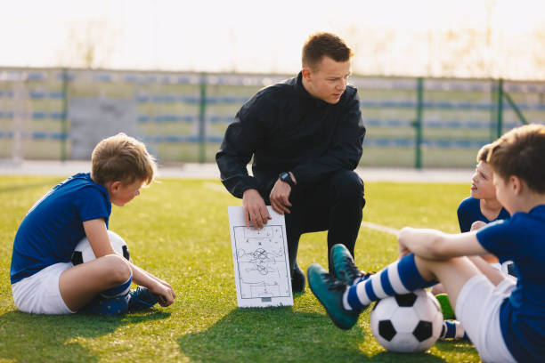 サッカーコーチは子供たちを指導します。子供のためのサッカーのトレーニングセッション。サッカー場で子供たちを教える若いコーチ。サッカーの戦術教育。コーチは、ゲームの戦略を説� - tutor ストックフォトと画像