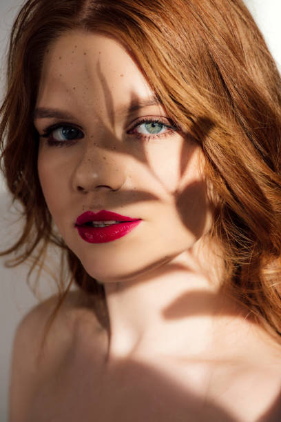 istock beautiful young redhead woman with red lips and shadow on face looking at camera 1148413101