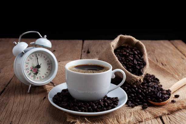 istock White Coffee cup with white alarm clock and coffee beans on old wood plank background 1148416920