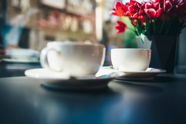 Two cups of coffee on table in cafe by window near vase with bouquet of pink tulips on sunny morning.