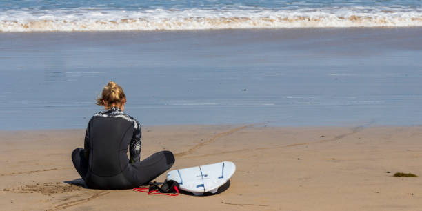 surfer mädchen sitzt am strand von la caleta. lanzarote. - famara stock-fotos und bilder
