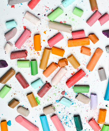 Background of many multicolored pastel crayons on a white background, top view