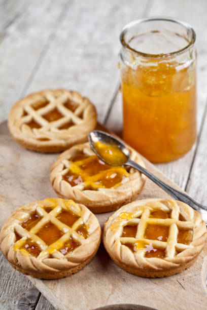 Fresh baked tarts with marmalade filling and apricot jam in glass jar on cutting board on rustic wooden table. Fresh baked tarts with marmalade filling and apricot jam in glass jar on cutting board on rustic wooden table background. crostata stock pictures, royalty-free photos & images