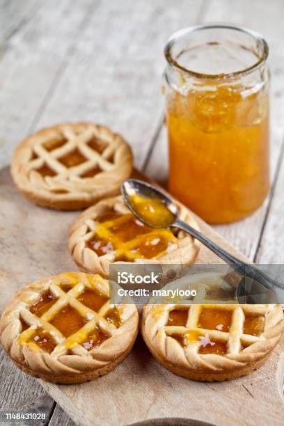 Fresh Baked Tarts With Marmalade Filling And Apricot Jam In Glass Jar On Cutting Board On Rustic Wooden Table Stock Photo - Download Image Now
