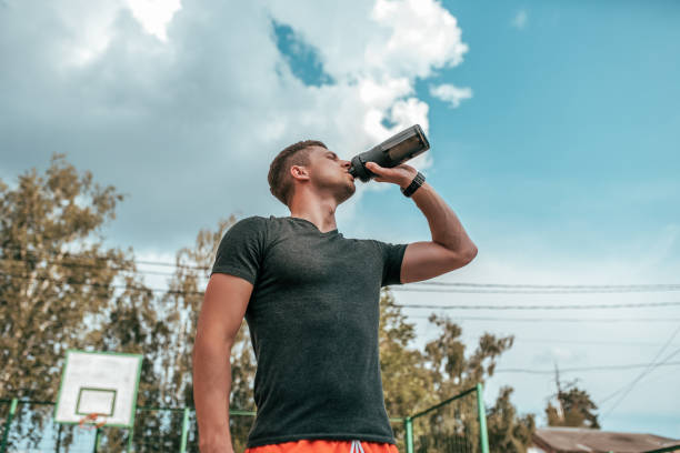 Male athlete, drinking water and protein from shaker, fitness watch, training in the city in the fresh air. Concept morning run in the city, fitness and workout, smart watch bracelet. Sportswear T-shirt. stock photo