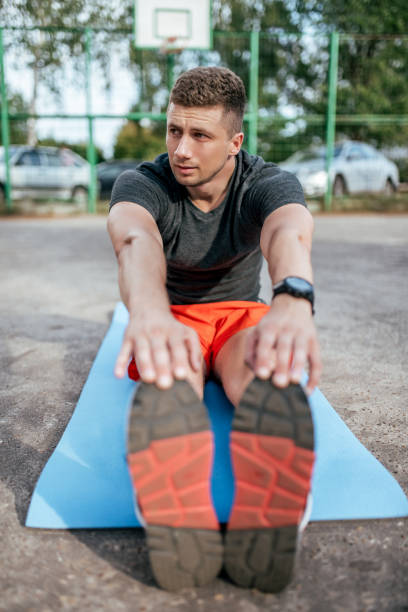 istock A male athlete doing gymnastics stretching muscles, training muscles flexibility plasticity on mat, in city fresh air. Fitness concept and workout, smart watch bracelet. Sportswear T-shirt shorts. 1148434036