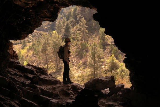 istock HIKER MAN AND ADVENTURER WITH HAT AND BACKPACK IN A CAVE LOOKING A VALLEY WITH GREEN TREES 1148437017