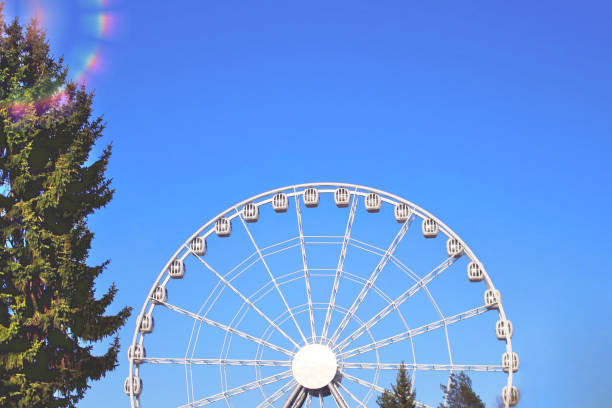 карусель притяжения ездить белое колесо обозрения в парке развлечений перед голубым небом - carnival spinning built structure frame стоковые фото и изображения