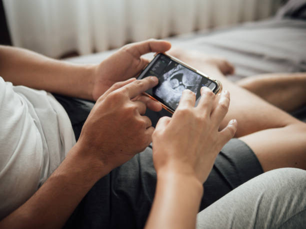 schwangere paar beobachtet ultraschall-video auf smartphone - human pregnancy telephone ultrasound family stock-fotos und bilder