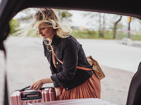 Woman packing her car with luggage bags ready for trip
Modern photo taken outdoors of woman and suitcases by car