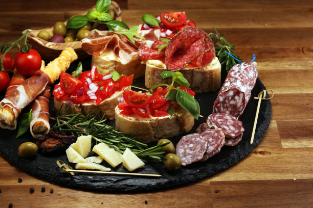 istock Traditional italian antipasto bruschetta appetizer with cherry tomatoes, cream cheese, basil leaves and balsamic vinegar on cutting board with prosciutto, salami, cheese 1148454202