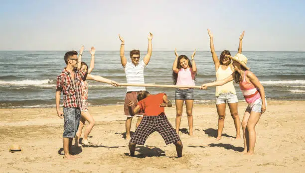 Multiracial happy friends group having fun together with limbo game at beach - Summer joy and friendship concept with young multi ethnic people playing on spring break vacation - Retro vintage filter