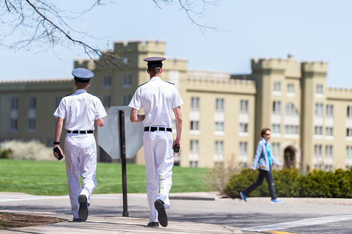 Lexington, USA - April 18, 2018: Men, male cadets students in white uniforms with phones walking at Virginia Military Institute main campus grounds in front of Clayton Hall
