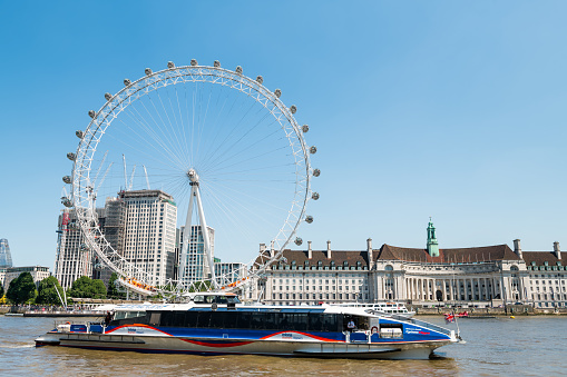 London, UK - June 25, 2018: Cityscape on Thames river with clippers ferry by London Eye, City Hall at Victoria Embankment in sunny summer