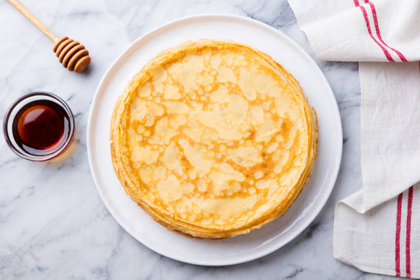 Crepes, thin pancakes with honey on a white plate. Marble background. Top view. stock photo