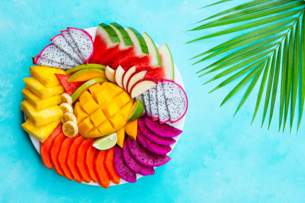 istock Tropical fruits assortment on a white plate with palm leaf. Blue background. Top view. Copy space. 1148465984