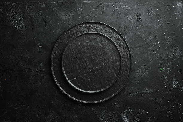istock Round black stone plate. On a black stone background. Top view. Free space for your text. 1148484104