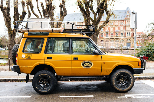 Strasbourg, France - Dec 27, 2017: Side view of Vintage new yellow Land Rover Defender Camel Trophy with luggage on the roof parked in central city street with
