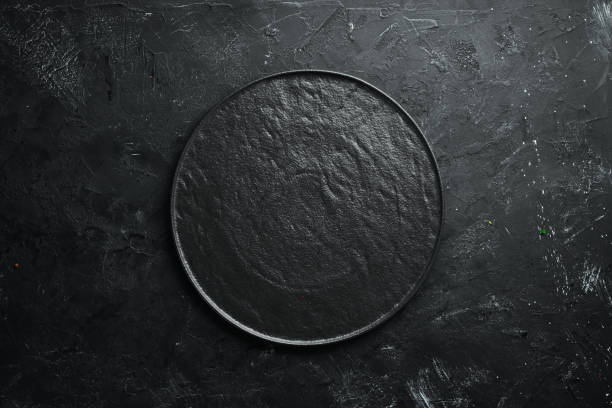 istock Round black stone plate. On a black stone background. Top view. Free space for your text. 1148495208