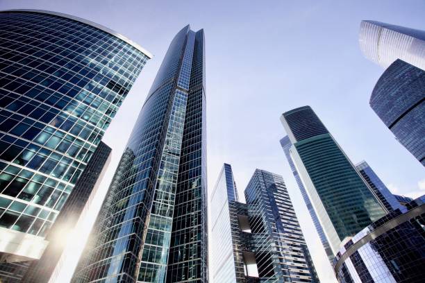 Office and residential skyscrapers against bright sun and clear blue sky Office and residential skyscrapers against bright sun and clear blue sky. Commercial real estate. Glass and metal in urban architecture. High-tech facade design. Modern business city district. Office buildings exterior. Financial city district. Reflections and highlights in glass. Wide angle city photography. commercial real estate stock pictures, royalty-free photos & images