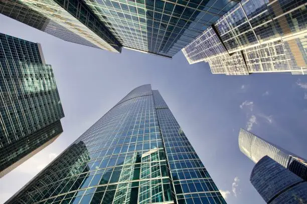 Office and residential skyscrapers against bright sun and clear blue sky. Commercial real estate. Glass and metal in urban architecture. High-tech facade design. Modern business city district. Office buildings exterior. Financial city district. Reflections and highlights in glass. Wide angle city photography.