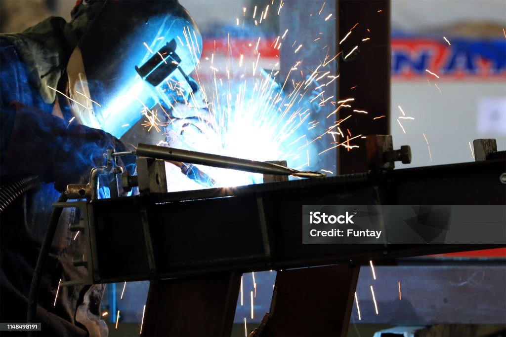 The welder is welding to structural steels with Gas metal arc welding (GMAW), also known as metal inert gas or MIG welding in the workshop. Welder Stock Photo