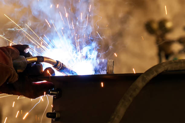 Close up view of the gas metal arc welding (GMAW), also known as metal inert gas or MIG welding. In addition to melting the base metal, a filler material is typically added to the joint to form a pool of molten material. vista de cerca de la soldadura por arco metálico a gas (gmaw), también conocida como gas inerte metálico o soldadura mig. además de derretir el metal base, se suele añadir un material de relleno a la articulación para formar un conjunto de material f