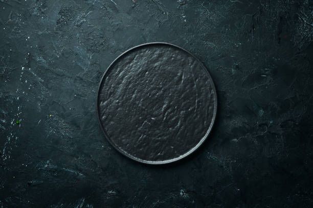 istock Round black stone plate. On a black stone background. Top view. Free space for your text. 1148498408