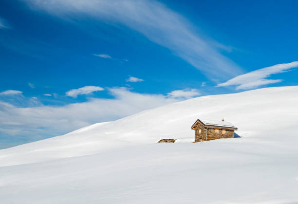 Panoramic view of snow covered slope on alpine mountain with remote small stone house residence