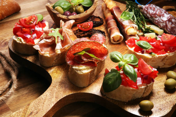 istock Traditional italian antipasto bruschetta appetizer with cherry tomatoes, cream cheese, basil leaves and balsamic vinegar on cutting board with prosciutto, salami, cheese 1148510012
