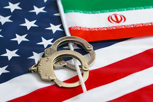 Iranian flag in handcuffs on the background of the American flag. US sanctions against Iran.