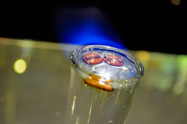 Cristal clear shot glass of flamed Sambuca liquor with coffee grains on a bar counter.