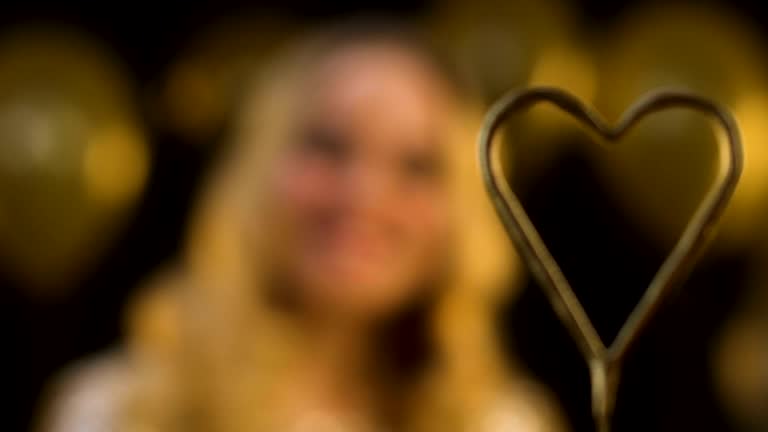 Heart-shaped bengal light, blond woman smiling on decorated background, party