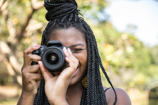 Young african woman taking photos with an DSLR Camera in the park