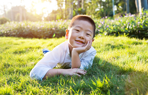 Smiling little asian boy lying on grass in park.