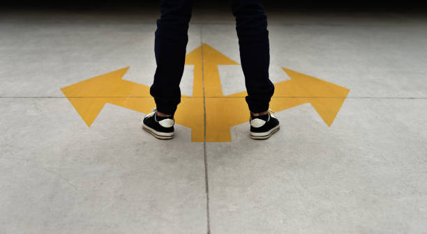 piedi giovani e tre frecce gialle dipinte sul pavimento - guidance confusion decisions one person foto e immagini stock