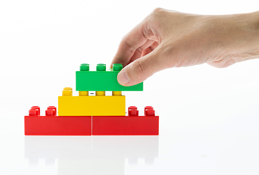 Human hand buildings toy bricks on white background.