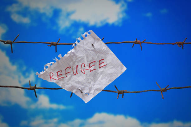 piece of paper with refugee text on barbed wire on blue sky background