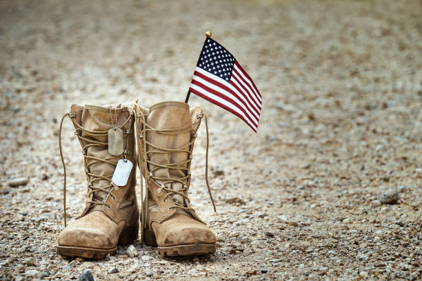 Old military combat boots with dog tags and a small American flag Old military combat boots with dog tags and a small American flag. Rocky gravel background with copy space. Memorial Day, Veterans day, sacrifice concept. boot stock pictures, royalty-free photos & images