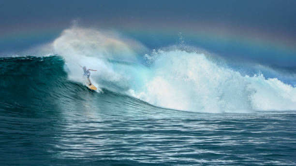 Surfer riding big green wave with rainbow in background in North Maluku islands, Indonesia Surfer riding big green wave with rainbow in background in North Maluku islands, Anbon, Halmahera sea, Indonesia ternate stock pictures, royalty-free photos & images