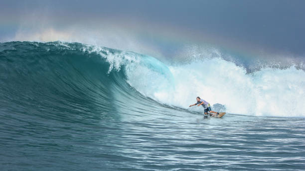 Surfer riding big green wave with rainbow in background in North Maluku islands, Indonesia Surfer riding big green wave with rainbow in background in North Maluku islands, Anbon, Halmahera sea, Indonesia ternate stock pictures, royalty-free photos & images