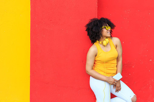 Smiling african woman standing in front of colored background and listening music.