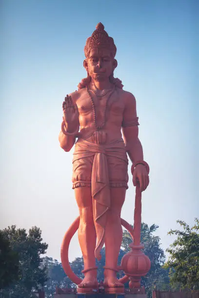 The view on a huge statue of red Hanuman with the raised hand in blessing gesture.