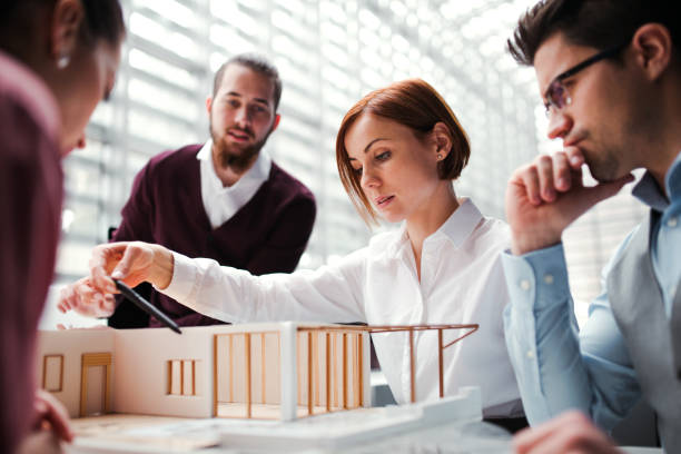 istock Group of young architects with model of a house working in office, talking. 1148580982