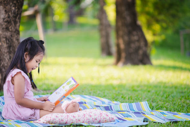 istock A little cute girl reading a book sitting under the tree 1148586353