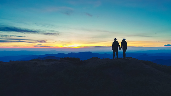The couple standing on the mountain on the sunset background