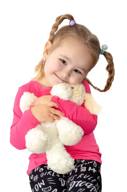 Pretty little girl with ponytails holding plushie dog doll isolated on white background. Adorable young smiling lady with stuffed toy. Cute girl hugging her teddy.